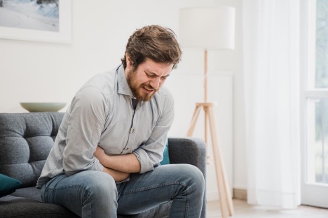 A man sitting on the sofa holding his stomach suffering from acid reflux